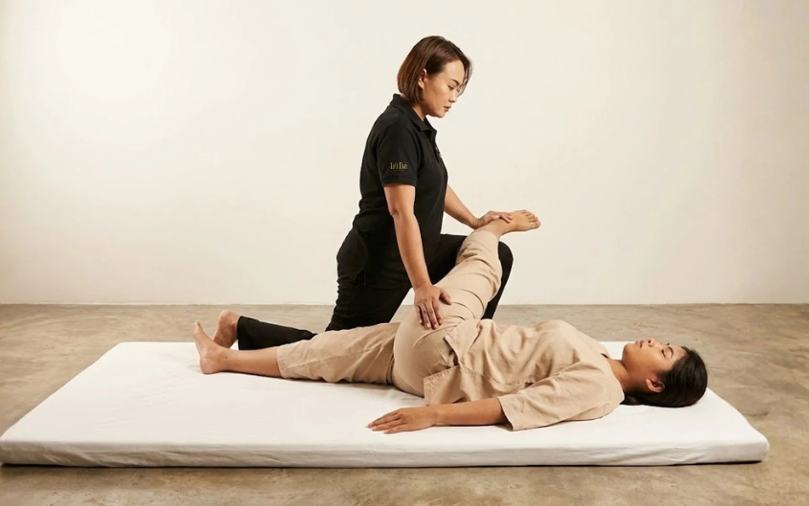 Thai massage therapist supporting a bent leg while applying broad palm contact to the inner thigh